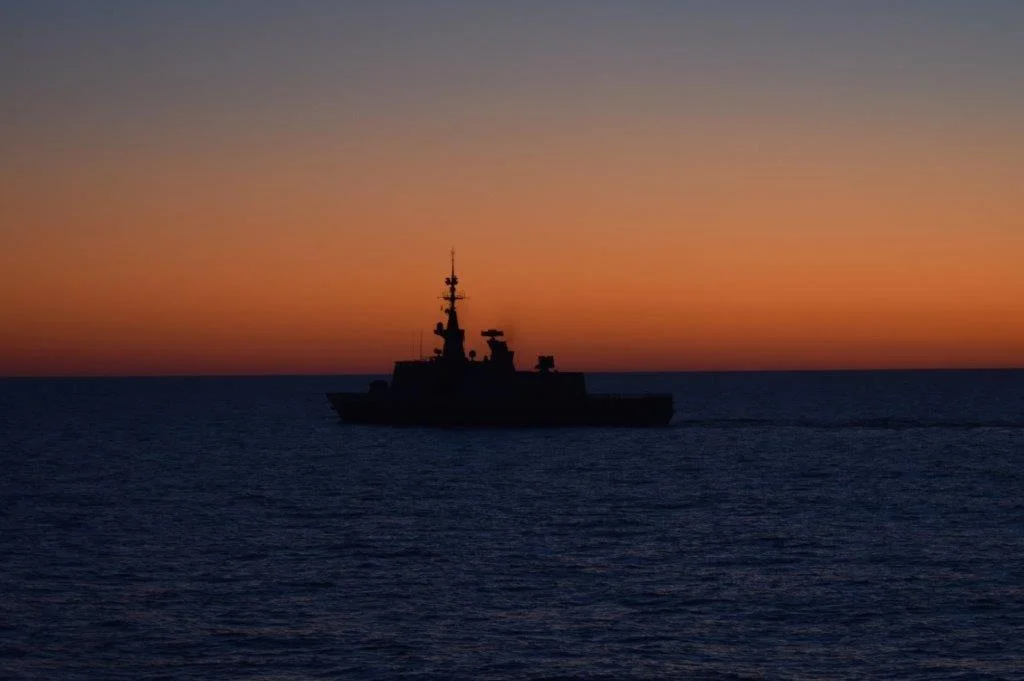 La frégate Aconit à contre-jour sur le soleil couchant