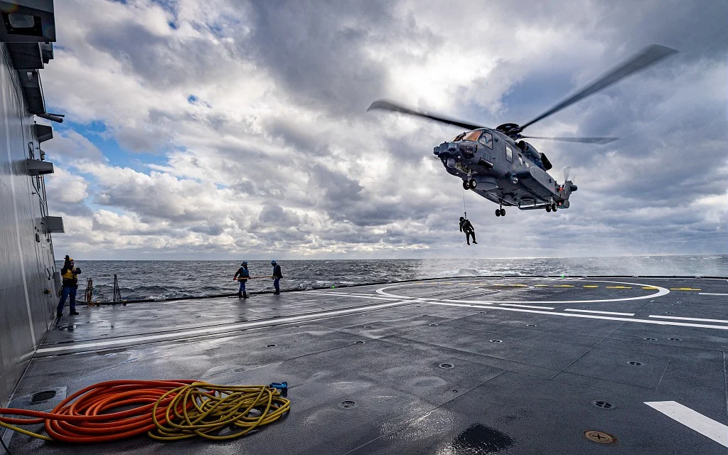 Un hélicoptère Caïman Marine (NH90) effectue un exercice de treuillage sur la plage arrière de la frégate Normandie