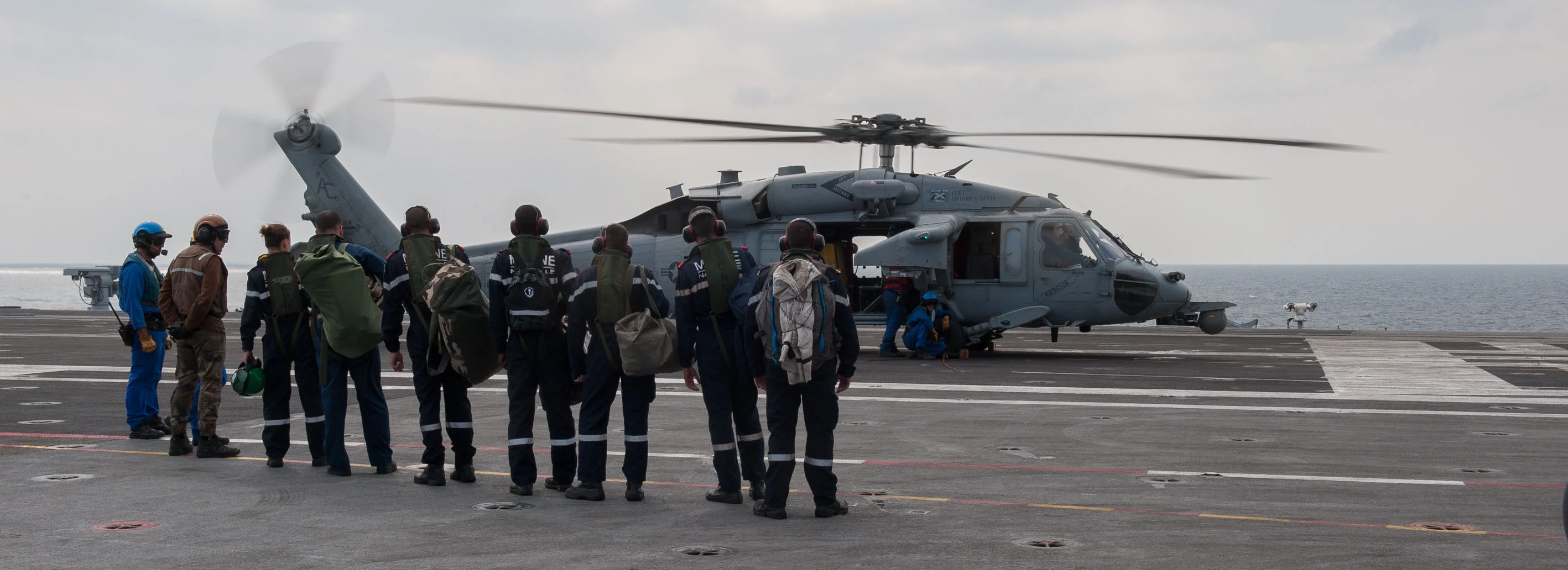 Des marins du Charles de Gaulle se préparent à embarquer à bord d'un hélicoptère américain MH-60R Sea Hawk pour rejoindre le porte-avions Harry S. Truman